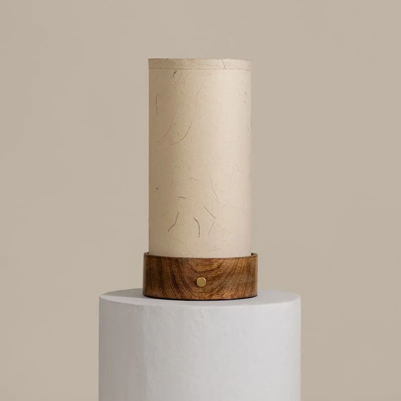 Ivory cylindrical table lamp with a wooden base on a white pedestal