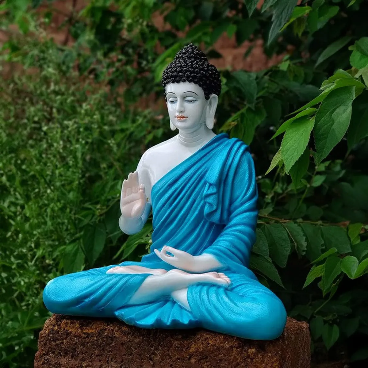 Side view of a blue and white Buddha idol seated in meditation outdoors