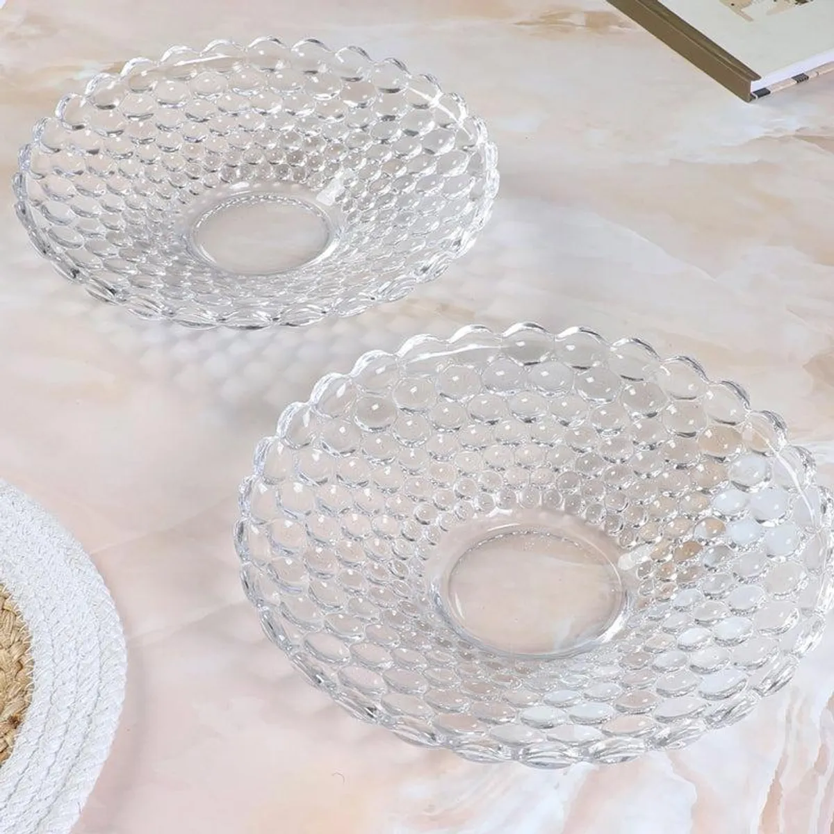 Two transparent bubble-textured glass platters displayed on a light tabletop