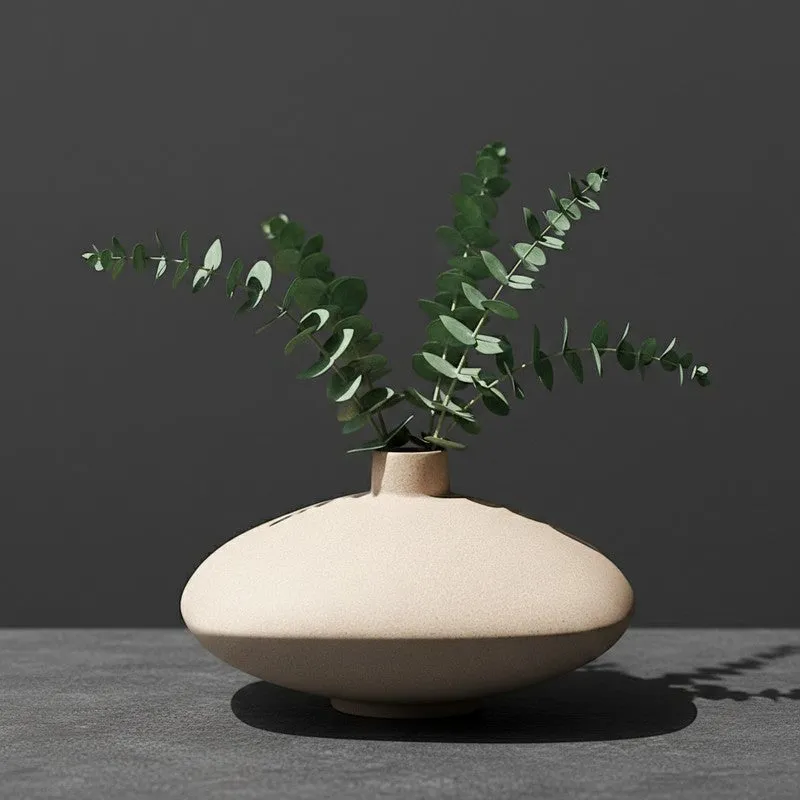 Ivory low bowl vase with eucalyptus stems on a dark background