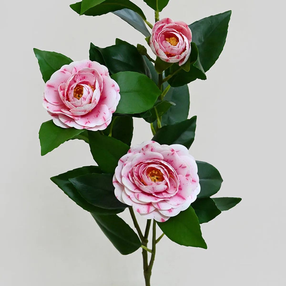 Close-up of three layered pink artificial rose blooms surrounded by dark green leaves