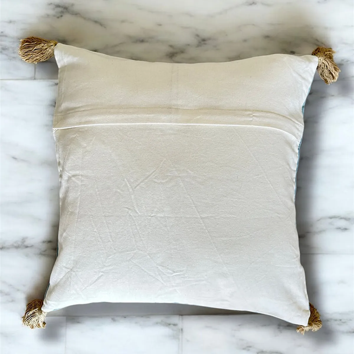 Back of a square cushion cover showing a plain light reverse and gold tassels