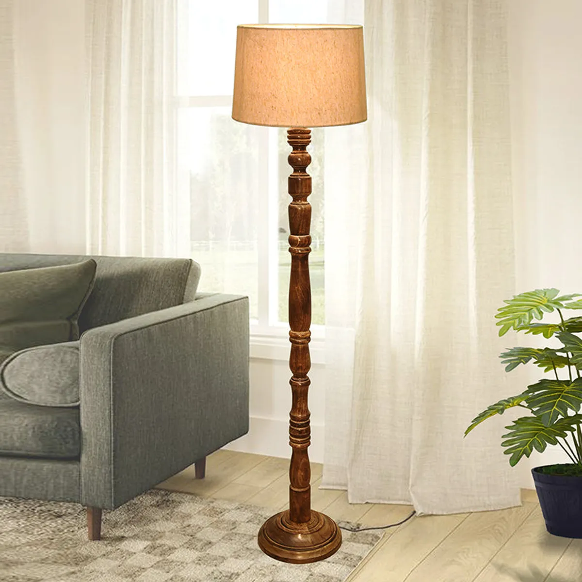 Wooden floor lamp with beige shade placed beside a sofa in a bright living room