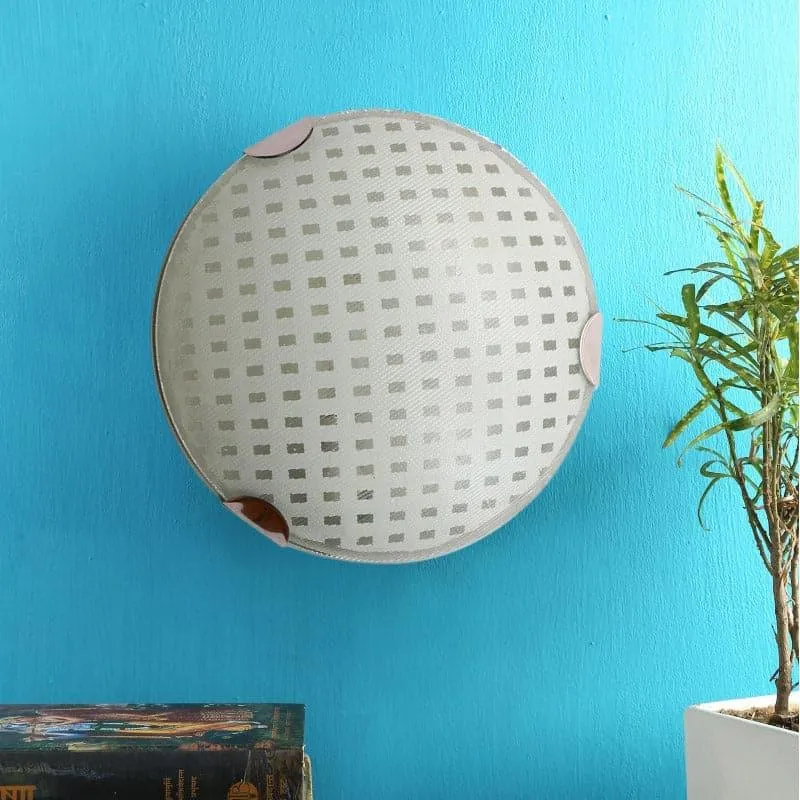 Unlit round white and silver wall lamp mounted on a blue wall beside a plant
