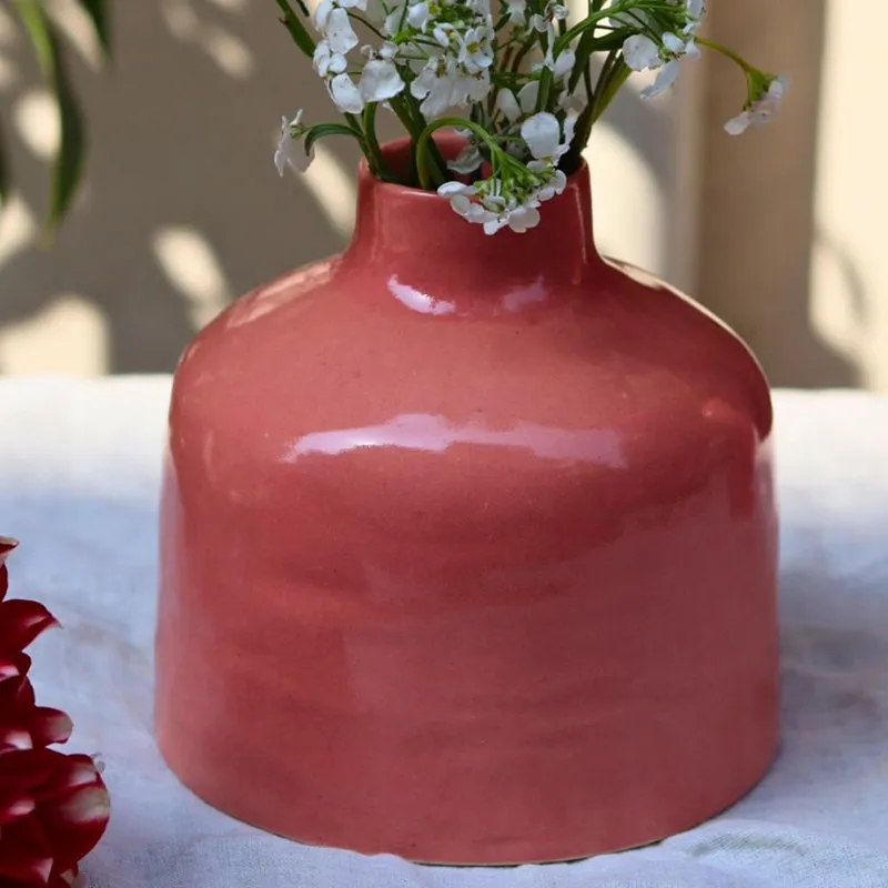 Close-up of a pink ceramic vase with white flowers on a draped surface.