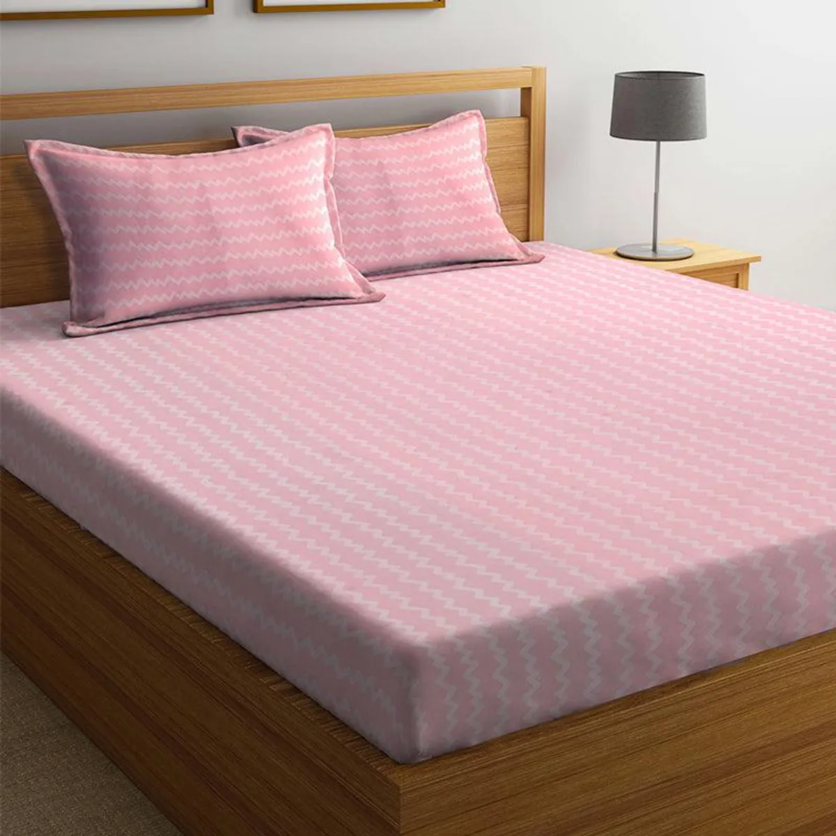 Pink geometric zigzag bedsheet and matching pillow covers on a wooden bed