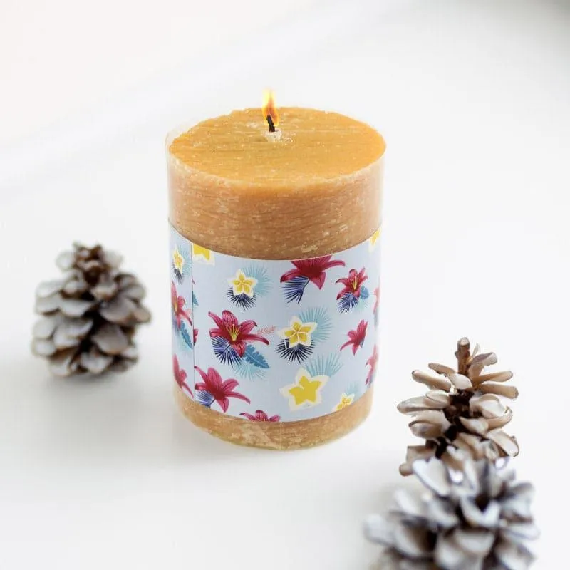 Lit brown pillar candle with floral wrap beside pinecones