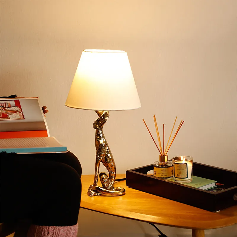 Gold table lamp with white shade styled on a wooden table beside books and candles