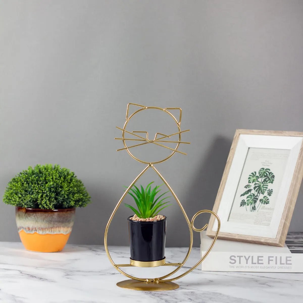 Gold cat-shaped planter with black pot styled on a marble surface