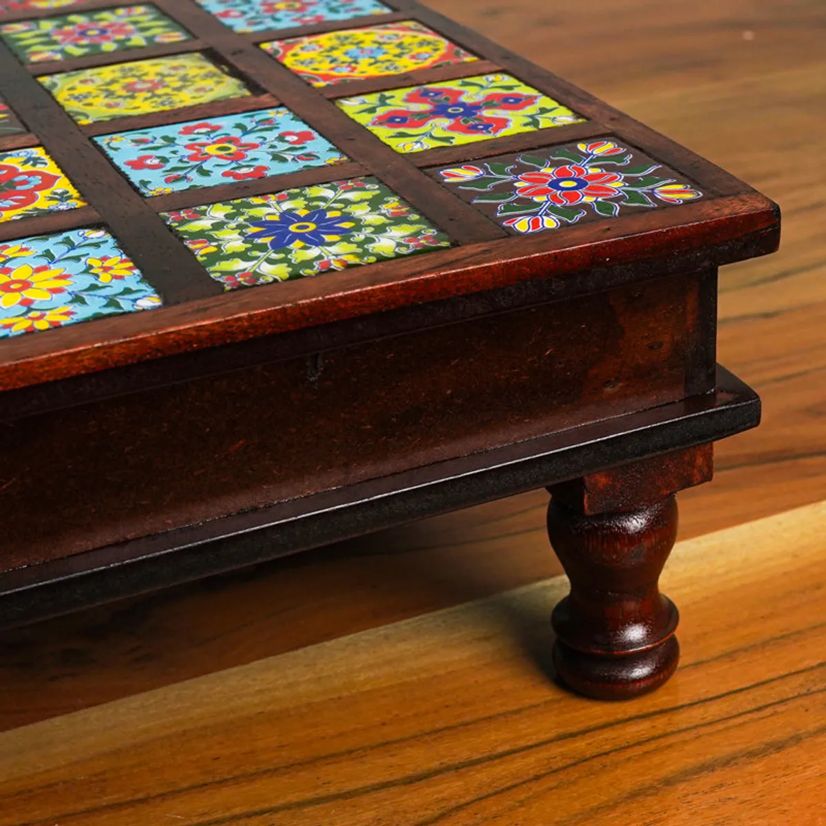Close-up of the stool's glossy dark wood edge, colourful tile motifs and turned leg