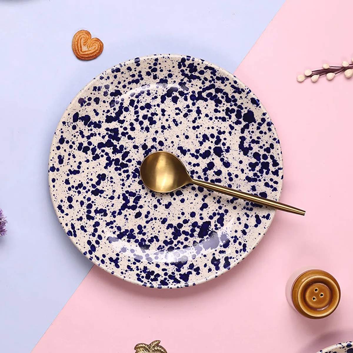Round blue splatter dinner plate with a gold spoon on a pastel backdrop