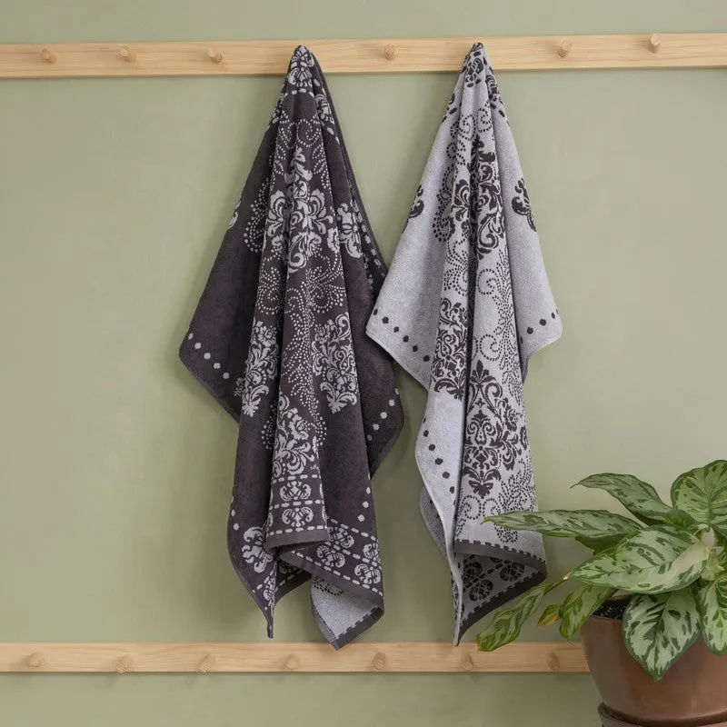Two grey floral bath towels hanging on a wooden wall rack