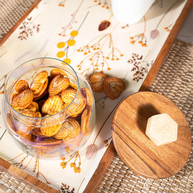 Open glass storage jar filled with cookies beside its round wooden lid