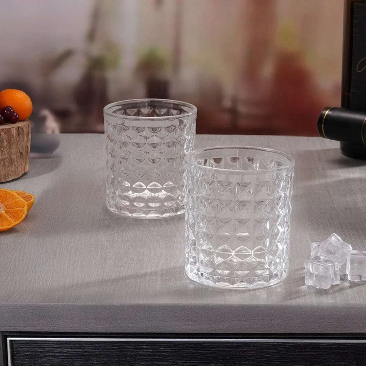 Two clear geometric-textured whiskey glasses with ice on a light table
