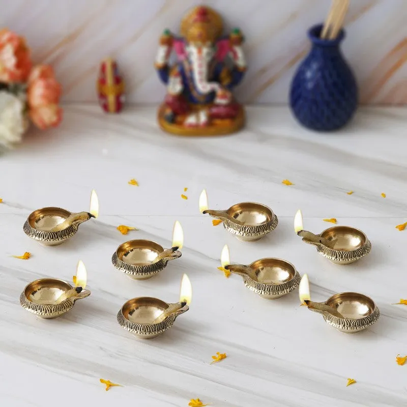 Eight gold brass diyas lit and arranged on a white surface
