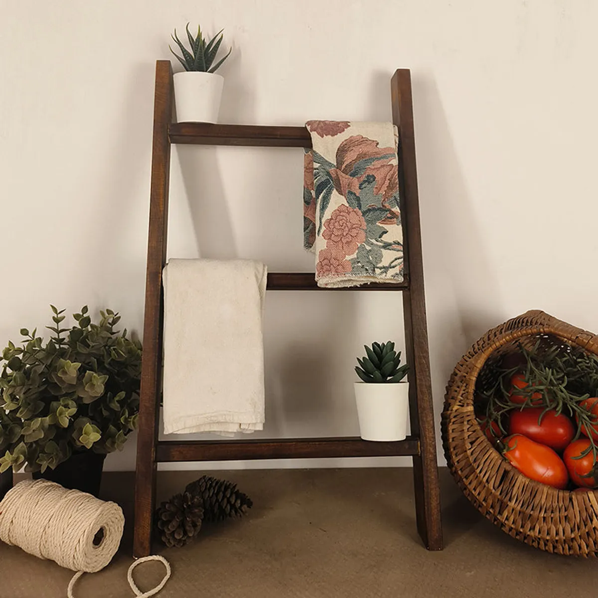 Brown wooden ladder-style rack styled with towels, a throw and small potted plants