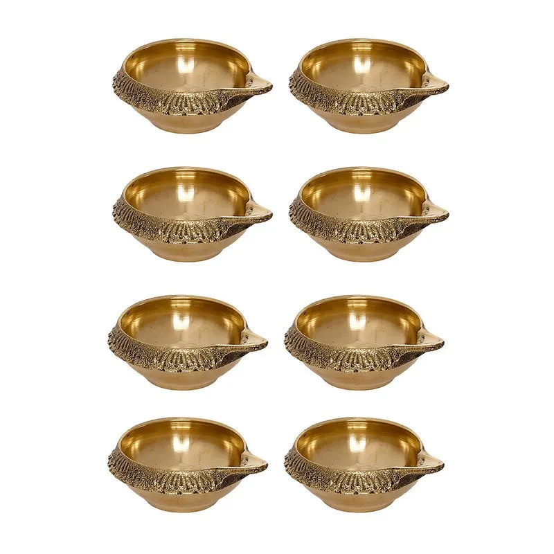 Set of eight gold brass diyas arranged in two columns on white