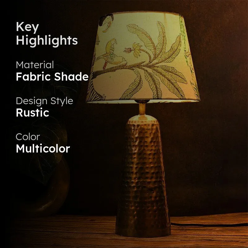 Table lamp with a tropical print shade and hammered metallic base against a dark backdrop