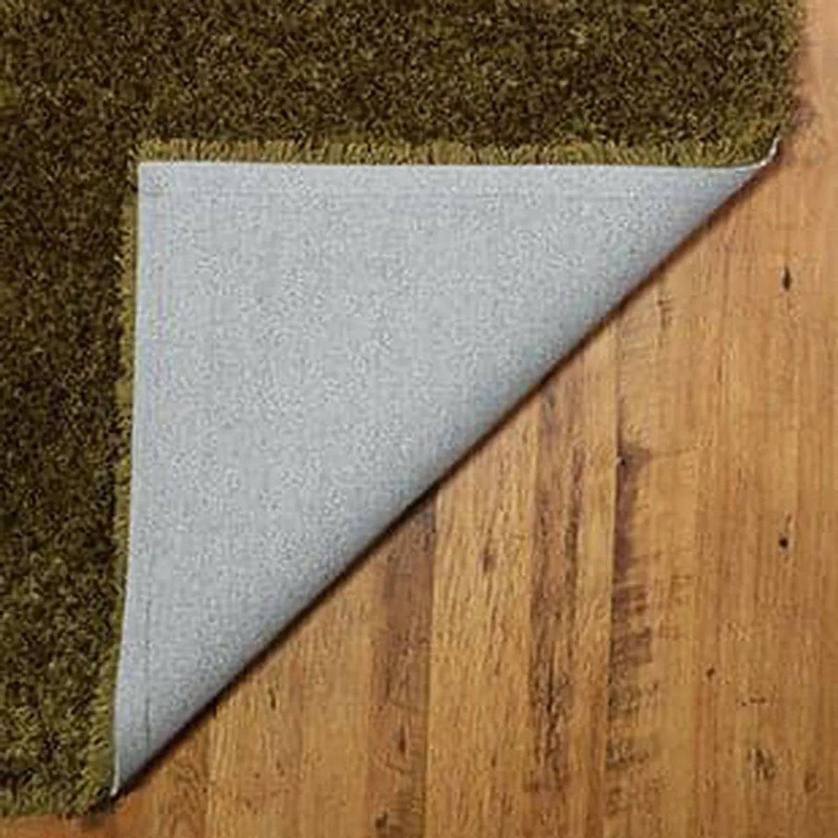Corner of the olive-green rug showing its light backing on a wood floor