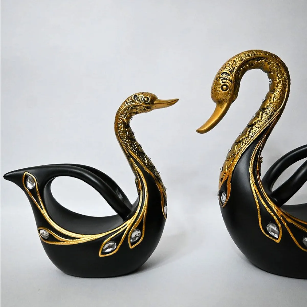 Close view of two black and gold swan showpieces with curved handles and crystal-like details.