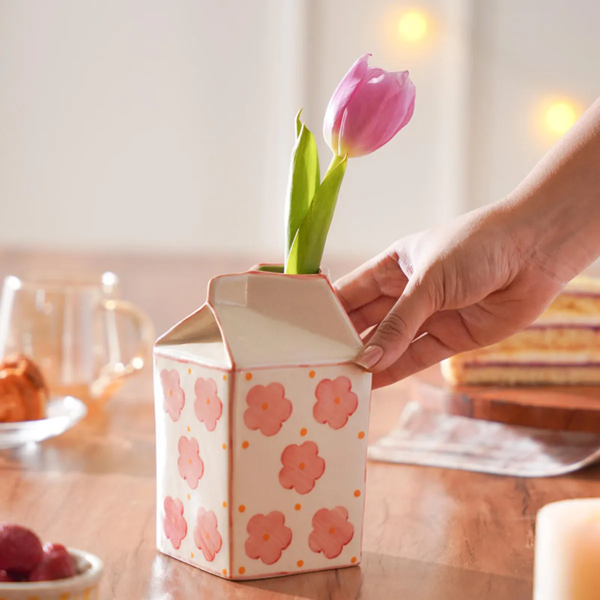 Hand placing a pink tulip into the floral carton-shaped vase
