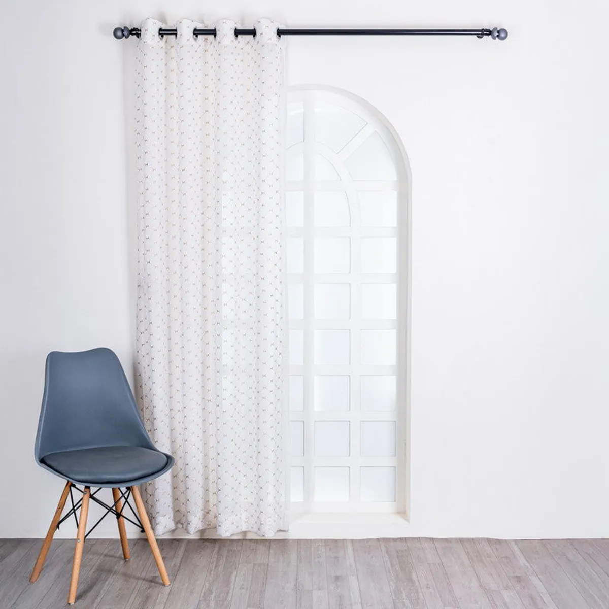 One sheer curtain panel covering an arched window in a bright room