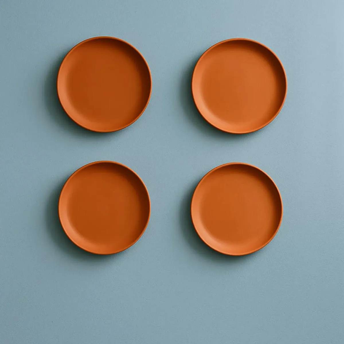 Four terracotta wall plates arranged on a pale blue wall