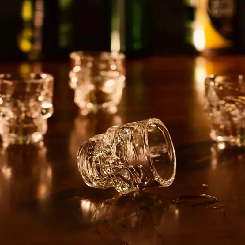 Clear skull shot glass lying on a dark table with other glasses in the background