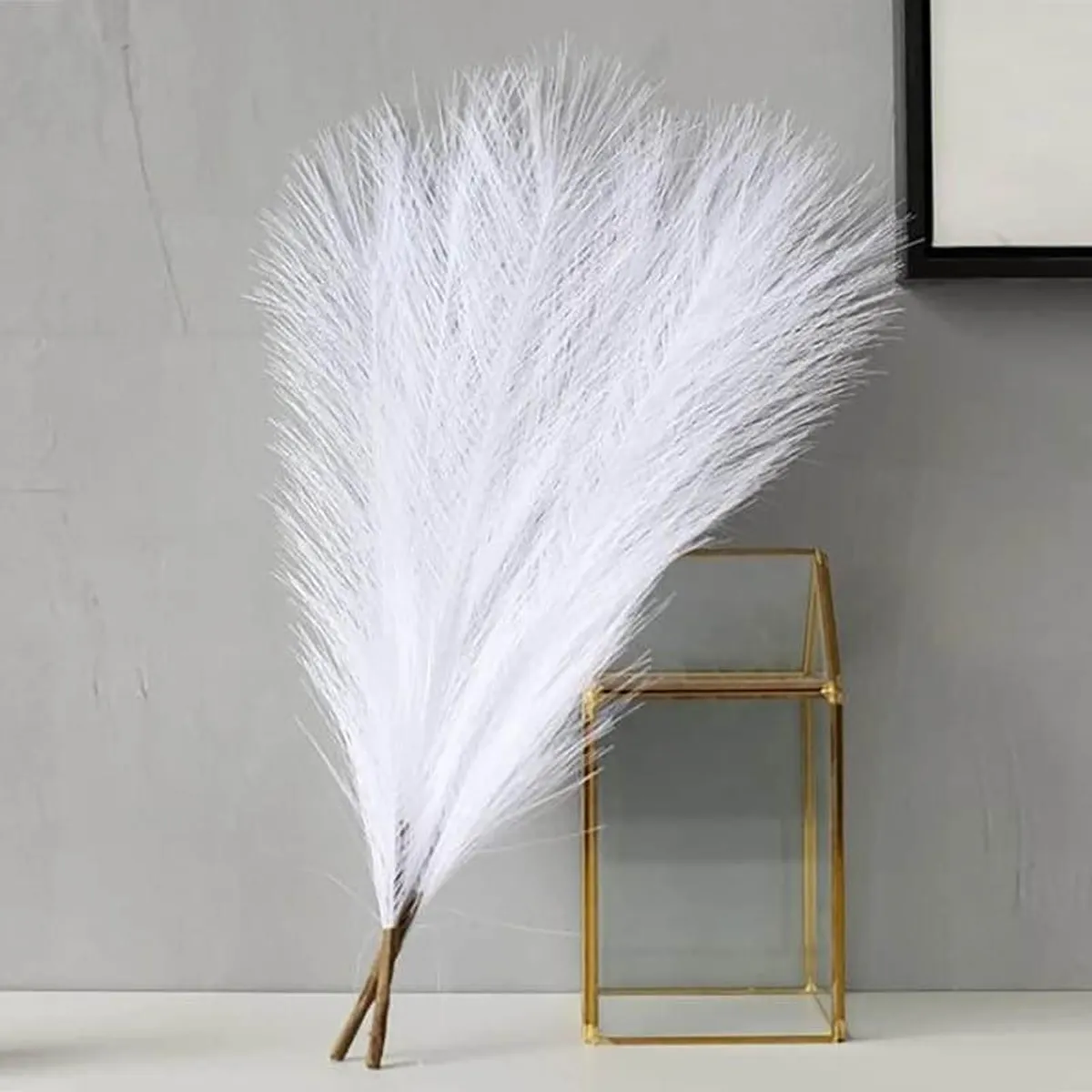 White fluffy faux pampas grass sticks displayed beside a gold glass box