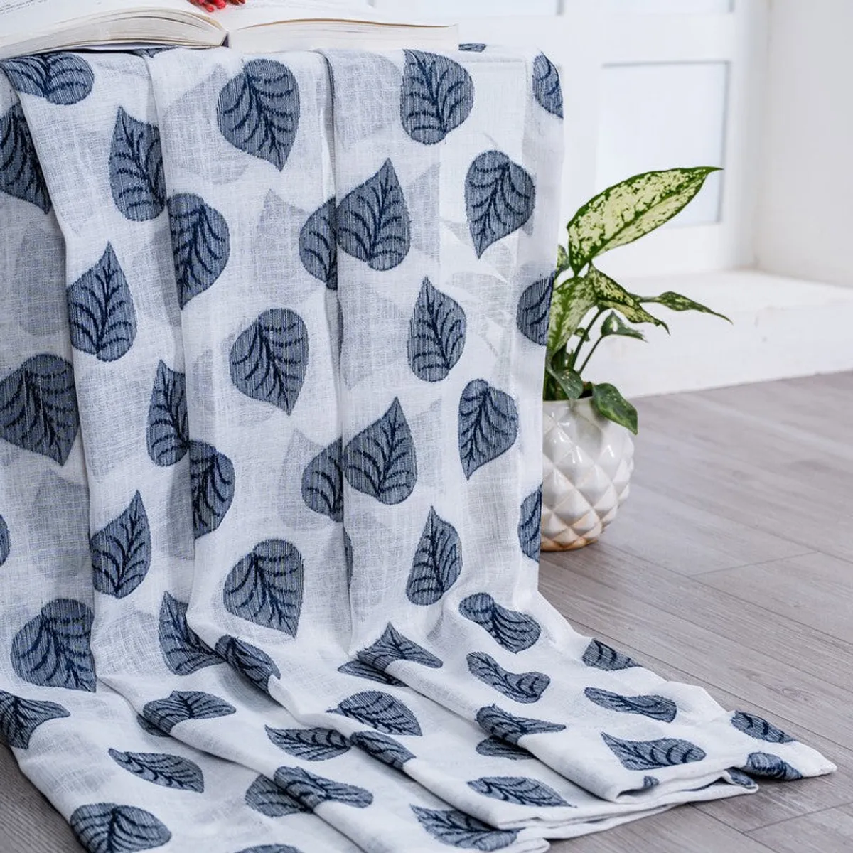 Leaf-patterned curtain fabric draped beside a plant and stool.