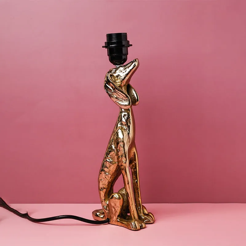 Close view of the gold sculptural lamp base with bulb holder against a pink background