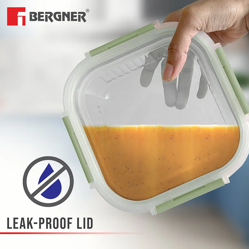 Hand holding a rectangular glass box with a green leak-proof lid and orange food