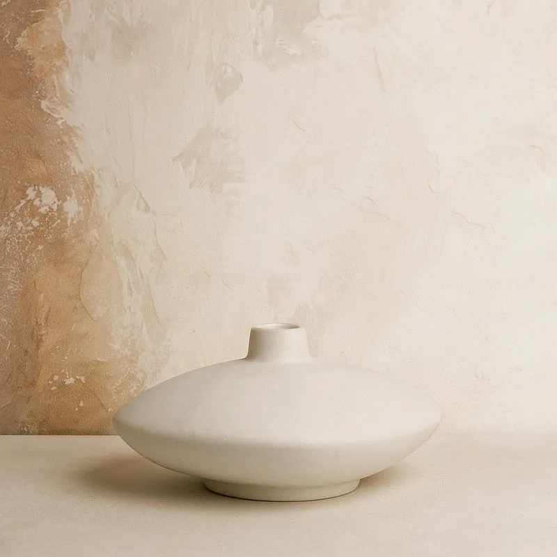Ivory low bowl vase against a textured beige wall