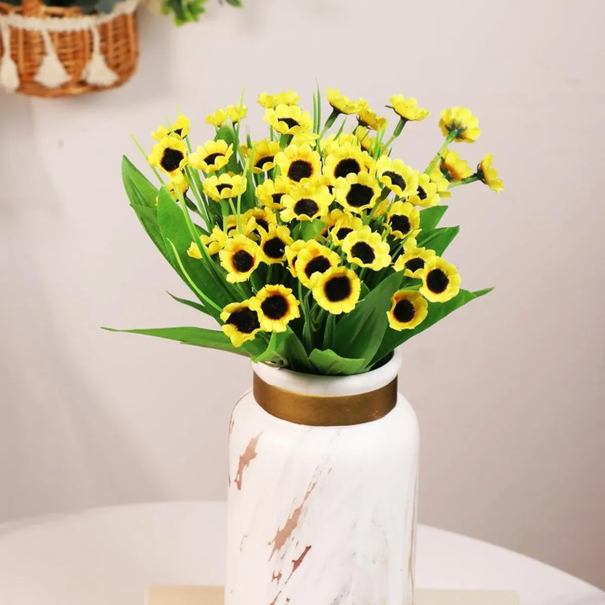 Yellow artificial sunflowers with green leaves displayed in a white decorative vase.
