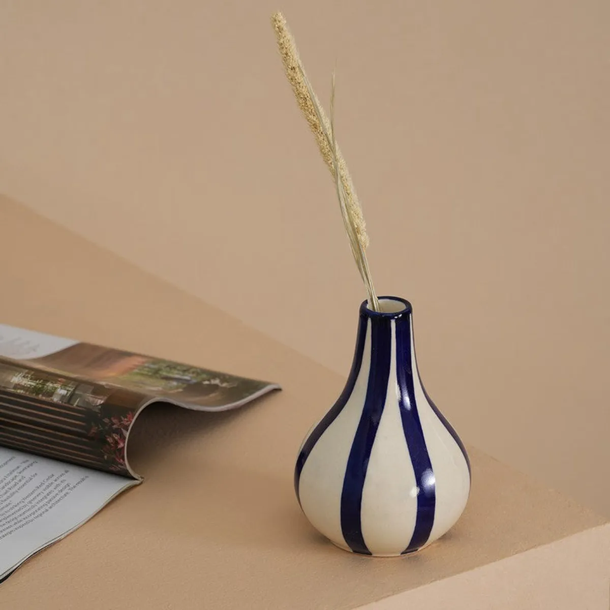 Blue and white striped ceramic vase styled with dried grass beside an open magazine