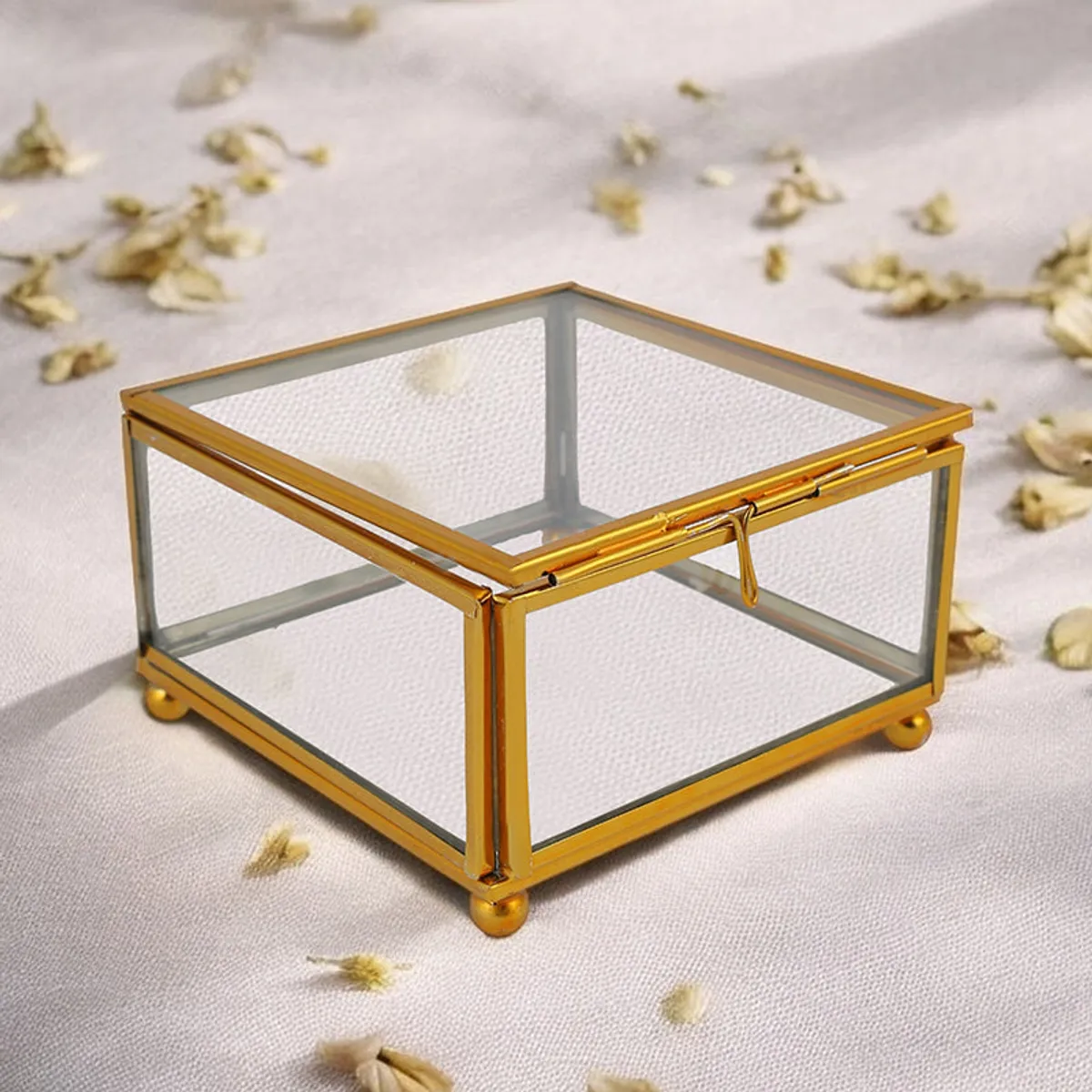 Gold-framed transparent glass jewel box styled on a light fabric surface