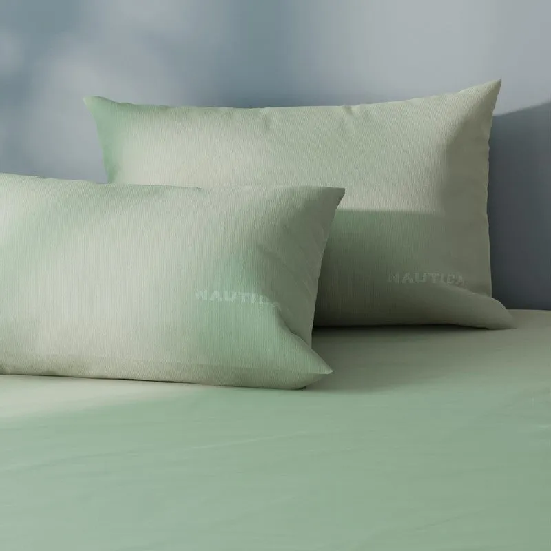 Soft olive green bedsheet and pillows shown in a close-up bedroom setting