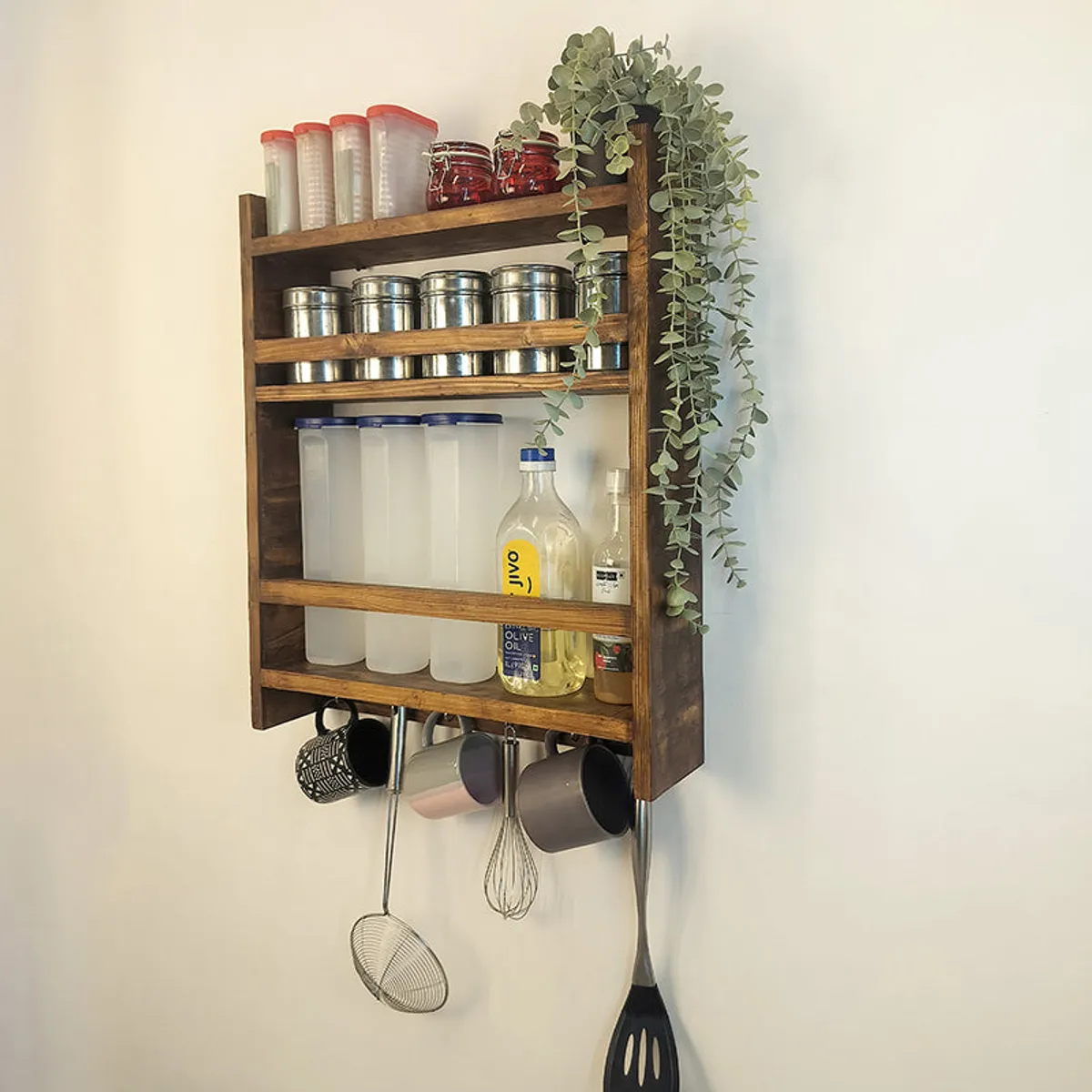 Brown wooden kitchen rack mounted on a wall with jars, containers and hanging utensils