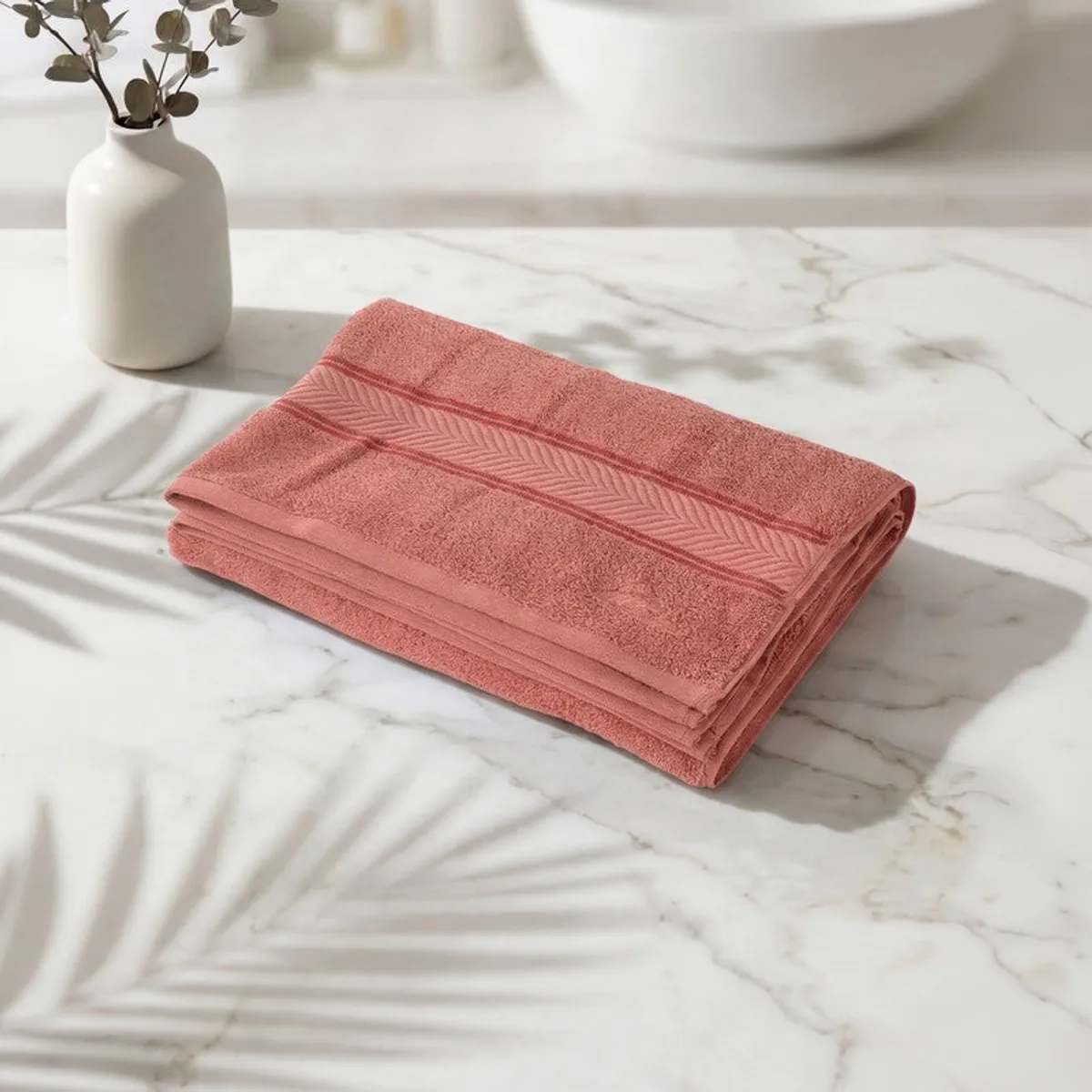 Folded peach bath towel showing a textured decorative border on a marble surface.