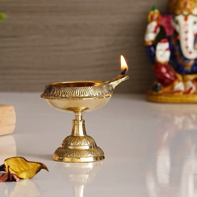 Single ornate gold brass diya with a lit wick displayed on a white surface.