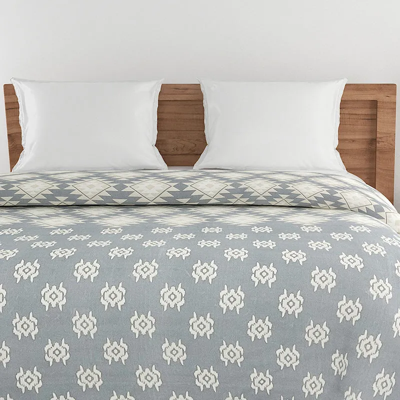 Grey comforter with white motifs folded over on a bed