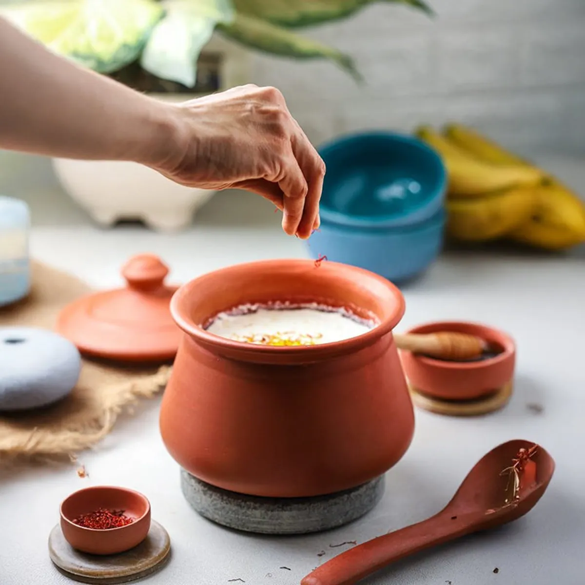 Terracotta handi with a creamy dish, spices and wooden serving accessories