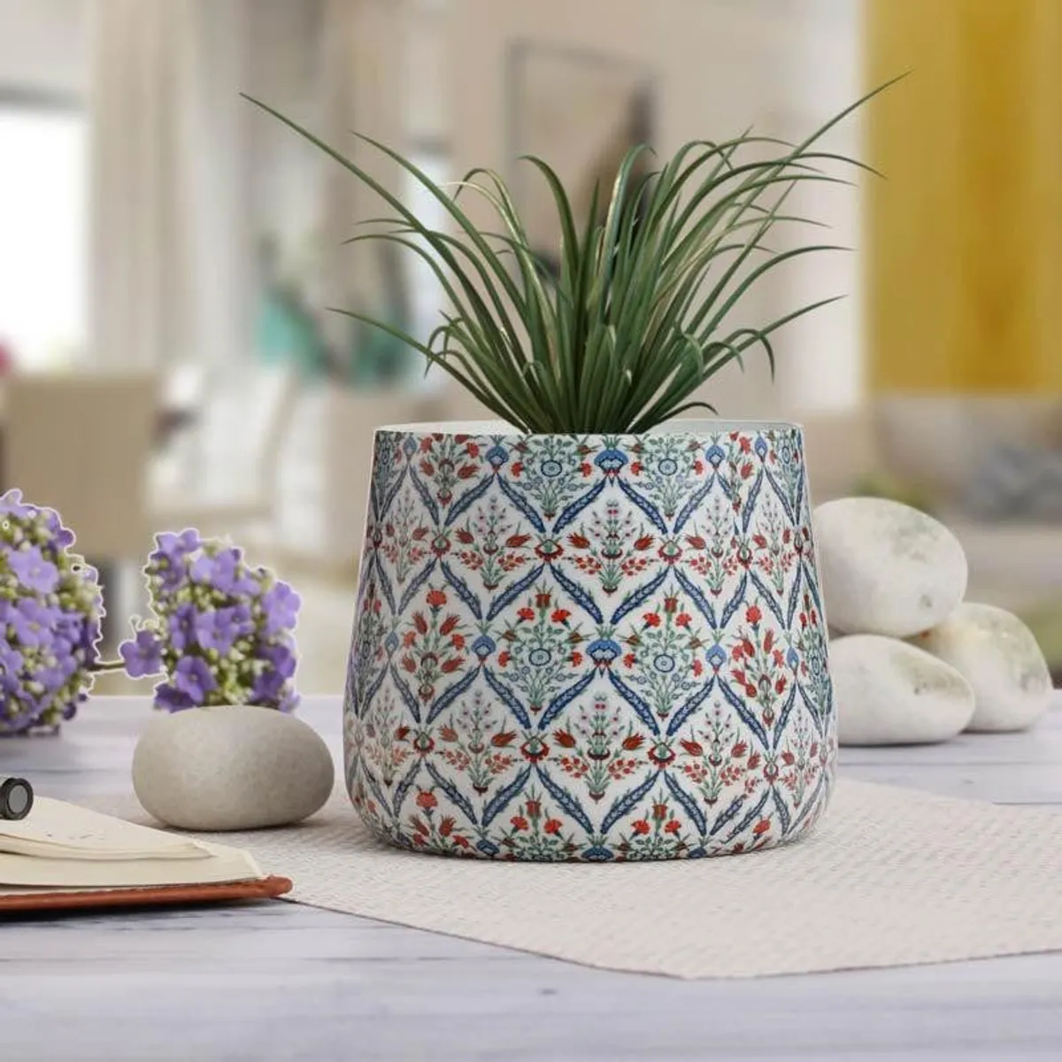Decorative floral planter holding a leafy plant beside smooth stones