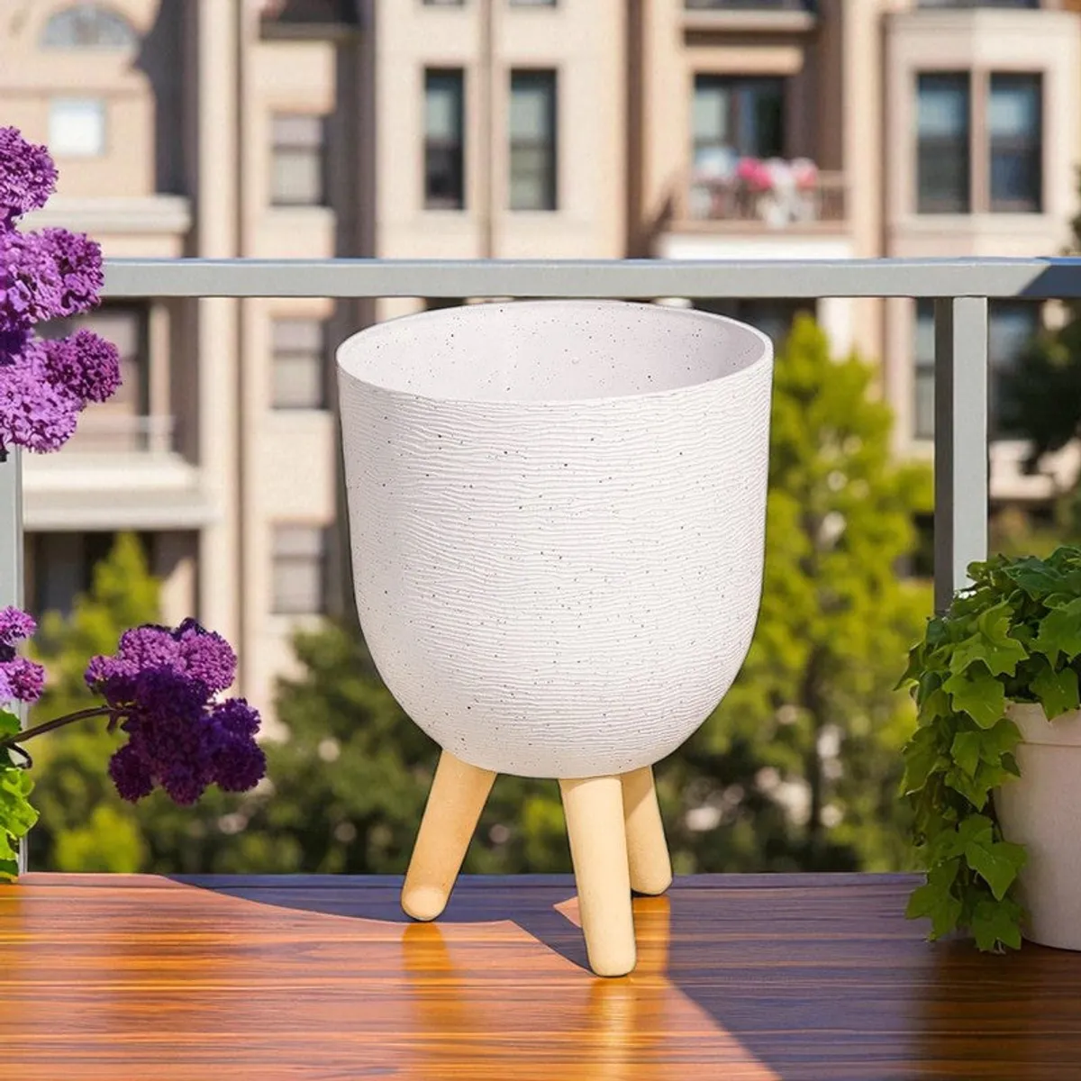 White planter on wooden legs displayed on a balcony with flowering plants.