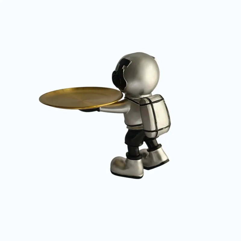 Side view of a silver astronaut figurine holding a gold tray