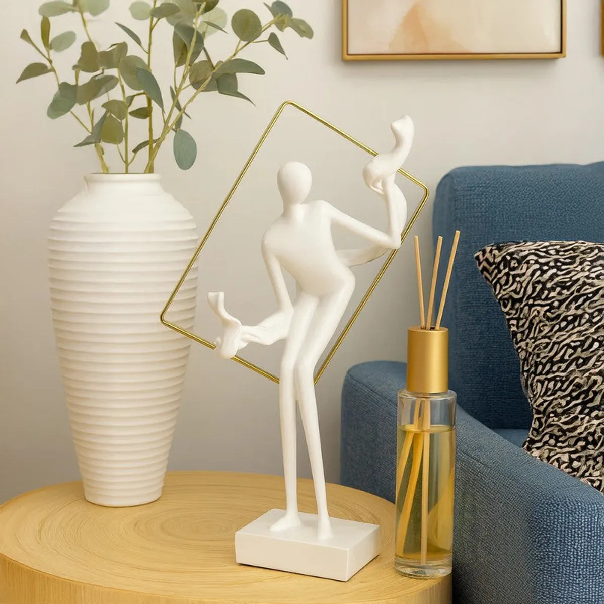White and gold abstract lady showpiece styled beside a vase and blue chair