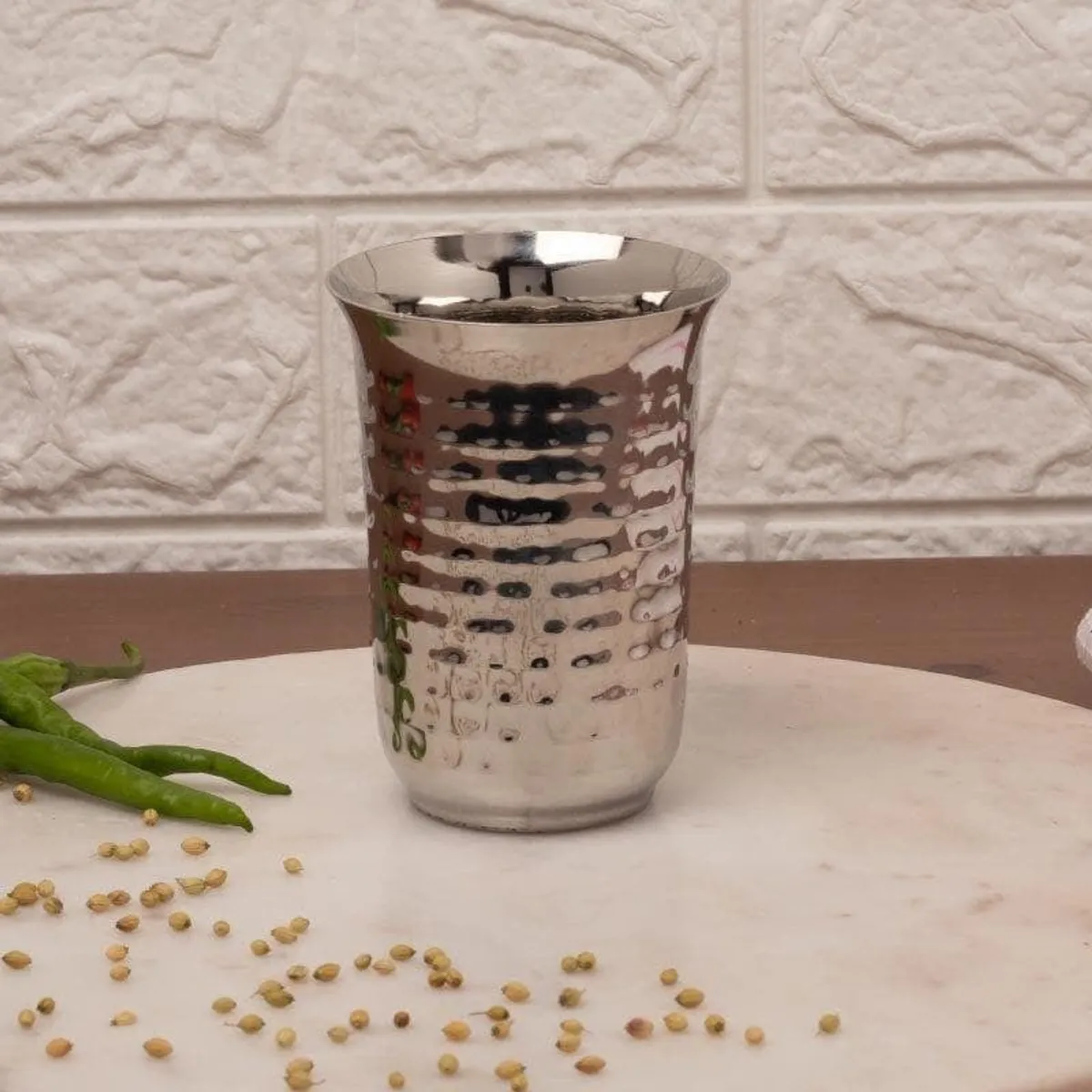 Single silver hammered drinking glass shown against a light textured wall