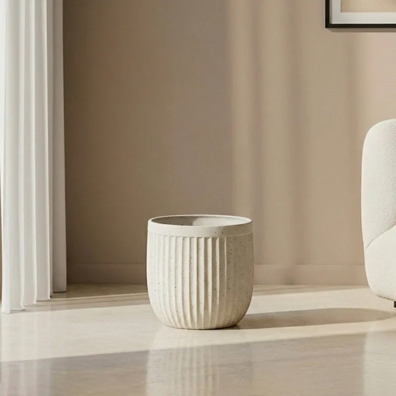 Small off-white ribbed planter displayed on a sunlit floor beside a sofa.