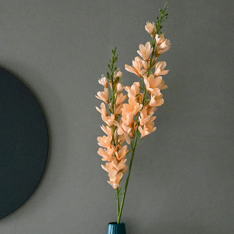 Ivory artificial flower stick with green stems displayed in a tall teal vase.