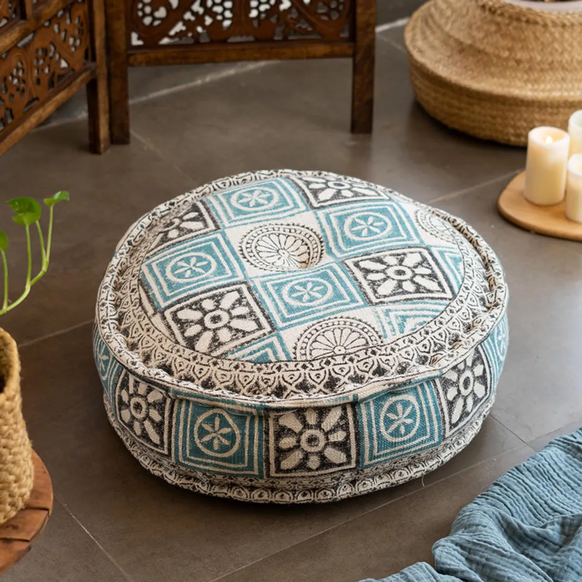 Round patterned floor cushion styled on a floor with a blue throw and candles.
